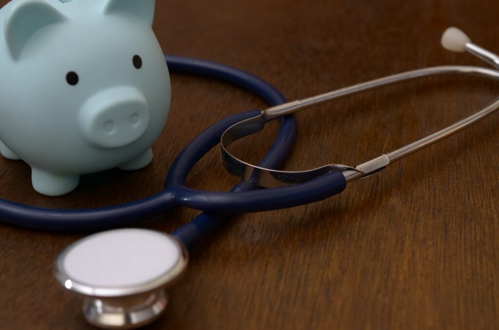 Blue piggy bank with medical stethoscope on wooden surface for healthcare costs concept