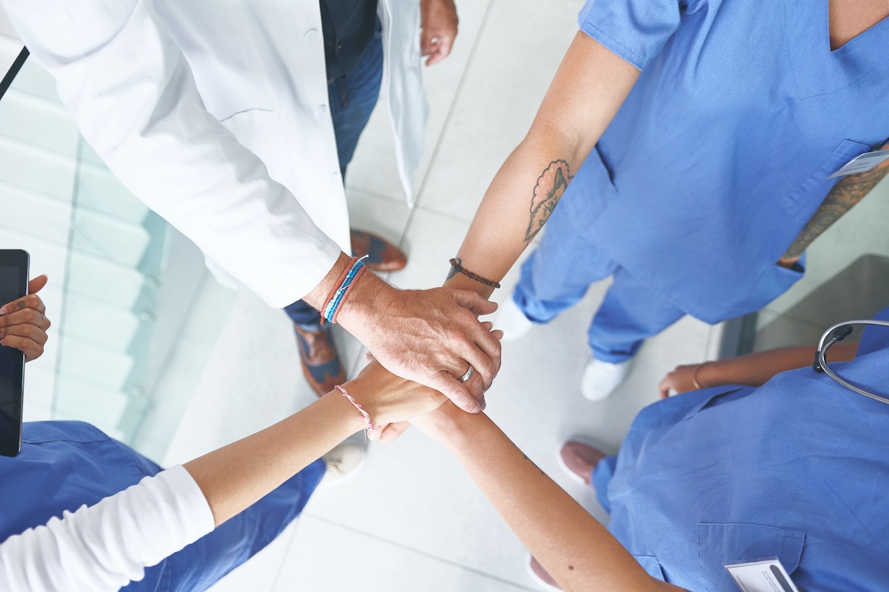 Hands together, above and meeting with doctors in hospital for solidarity, synergy and healthcare. Medical, teamwork and commitment with people in clinic for insurance, community and collaboration